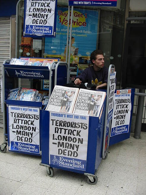 a man sitting behind a stand with newspapers reporting 