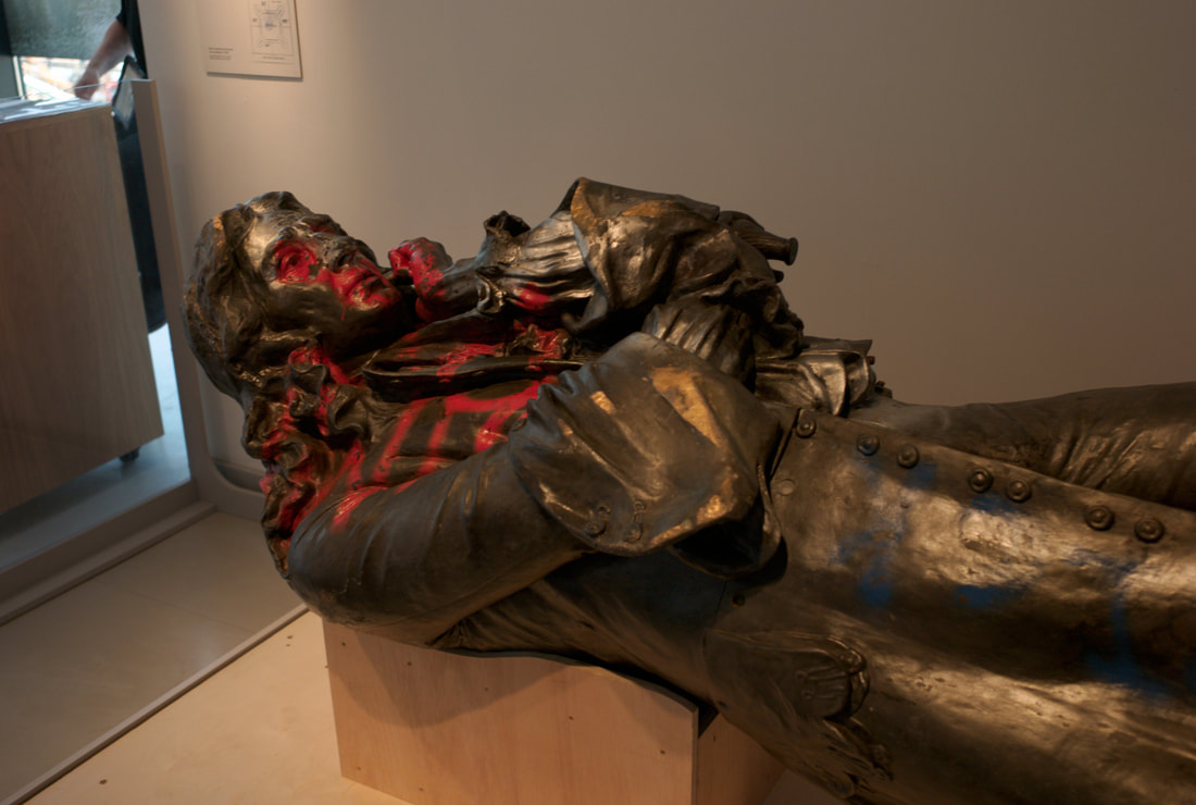 a bronze statue of a man in a room lying on its back with red paint on it