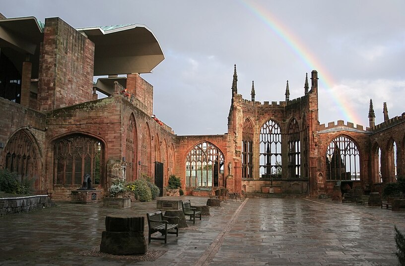 the remaining curated/preserved  walls of a brick religious building with benches and paving stones, and rainbow over the top