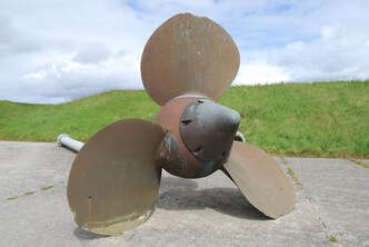 A metal propeller on a stone with grass in the background
